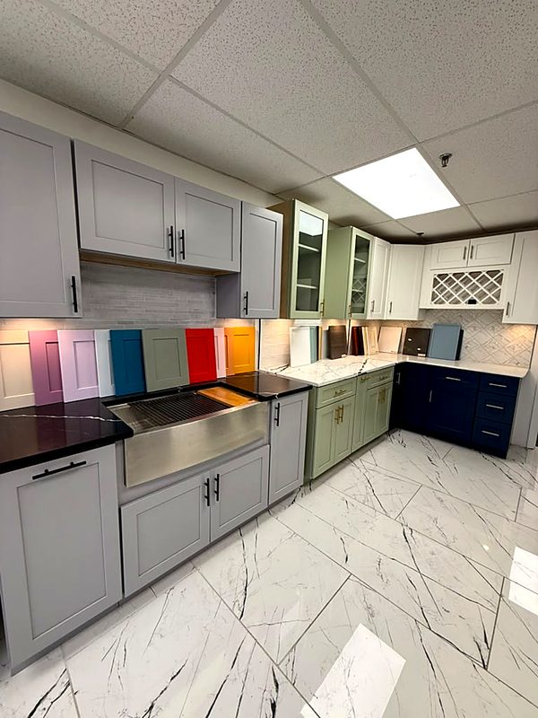 Wide showroom corner: light-gray shaker uppers and bases with black quartz counter and — on display at MNK Cabinet's Norcross, GA showroom
