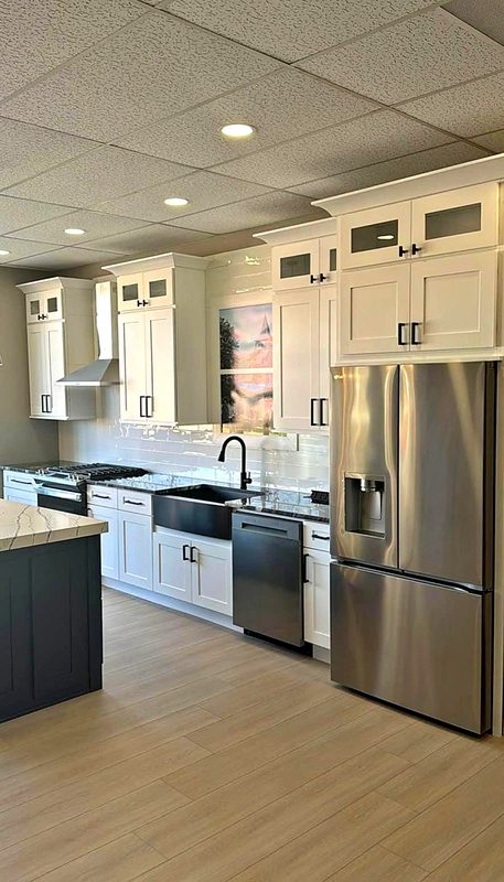 White shaker cabinets with glass-front stacked uppers, charcoal navy shaker island with — on display at MNK Cabinet's Norcross, GA showroom