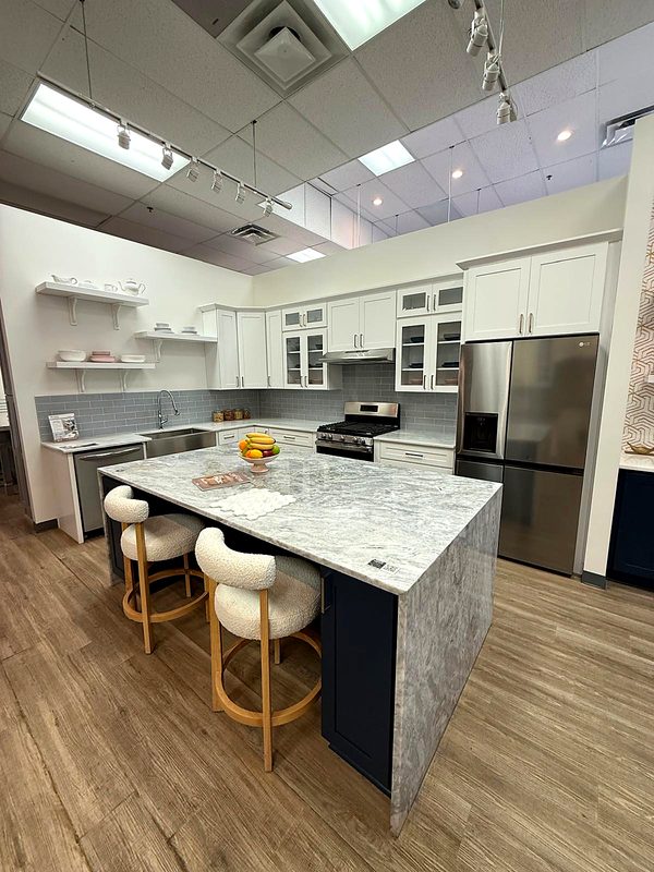 Full kitchen vignette: white shaker perimeter with glass-front uppers, navy blue shaker — on display at MNK Cabinet's Norcross, GA showroom