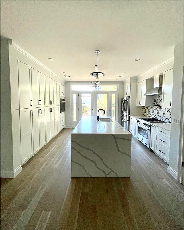 Bright galley kitchen with floor-to-ceiling white shaker pantry wall (black pulls) — kitchen by MNK Cabinet in metro Atlanta